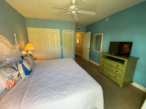 Un dormitorio con cama, almohadas, un televisor sobre un aparador y un ventilador de techo.
