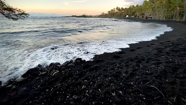 Une plage de sable noir, avec des vagues et des palmiers.