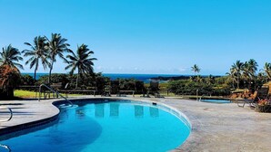 Ein Pool mit gewölbter Kante, umgeben von Liegestühlen und Palmen, mit Blick auf den Ozean.