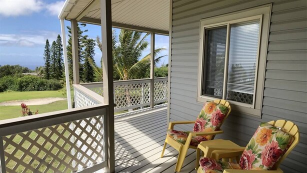A covered porch with two Adirondack chairs, a lattice railing, and a view of a golf course. - 2 Bedroom / 2 Bath Home on Golf Course with Stunni (Naalehu)