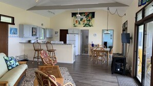 A spacious living area with a sofa, chairs, a dining table, and a kitchen in the background. - 2 Bedroom / 2 Bath Home on Golf Course with Stunni (Naalehu)