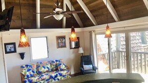 A kitchen with a wooden ceiling, a colorful floral sofa, a black chair, and pendant lights. - #56 Colony One at Sea Mt. Punalu`u (Pahala)