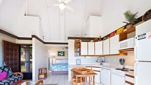 A modern kitchen with white cabinets, a dining area with a glass table, and a living room with a sofa and a TV. - #04 Rest & Relax at Punalu`u Black Sand Beach (Pahala)
