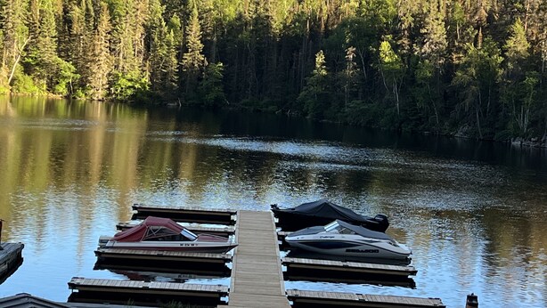 A dock with boats and a forested lake. - Lake Onaping Lodge (Unorganized North Sudbury)