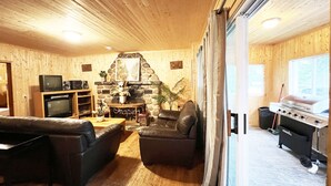 A wooden-paneled living room with a fireplace, leather sofas, a television, and a grill. - Lake Onaping Lodge (Unorganized North Sudbury)