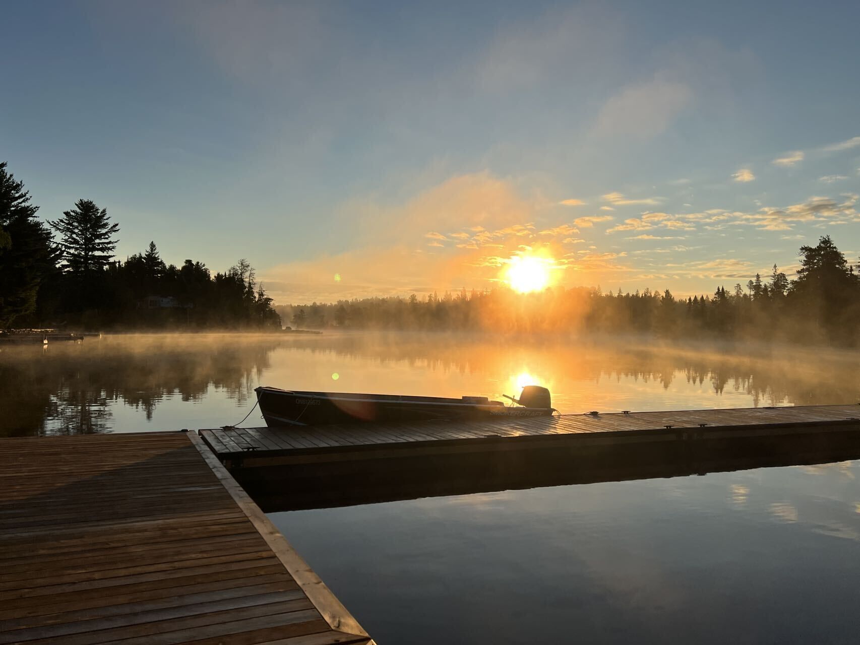 A wooden dock extending into a calm lake with a boat moored at the end.