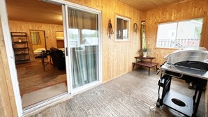 A wooden cabin with a sliding glass door leading to a living area, a grill, and a small table with a plant. - Lake Onaping Lodge (Unorganized North Sudbury)