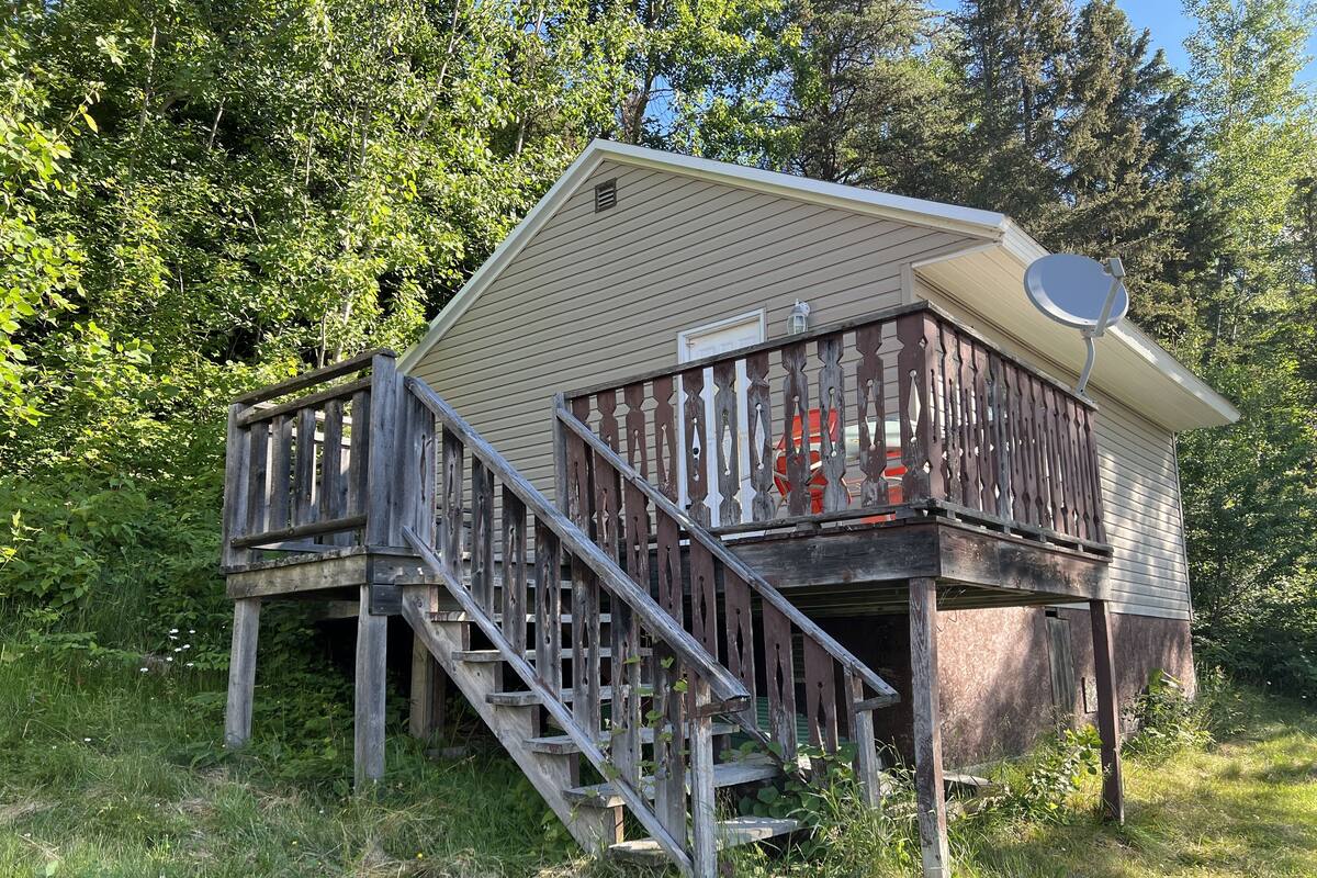 A wooden cabin with a balcony, a satellite dish, and a staircase leading to the entrance.