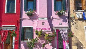 A pink building with a sign reading "Pink Paradise," featuring a tiled patio with pink furniture and potted plants. - Pink Paradise (Venezia)