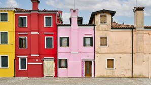 A row of colorful buildings with multiple windows and doors, a cobblestone street, and a clear sky. - Pink Paradise (Venezia)