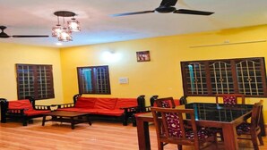 A room with a wooden floor, a dining table with chairs, a sofa set, and a ceiling fan.