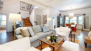 A spacious living room with a large gray sofa, a glass coffee table, and a staircase leading to another level. - Seabrook Exclusives | 2717 Seabrook Island Rd (Seabrook Island)