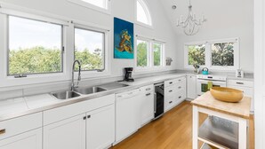 A modern kitchen with white cabinetry, a large window, and a wooden dining table. - Seabrook Exclusives | 2248 Rolling Dunes (Seabrook Island)