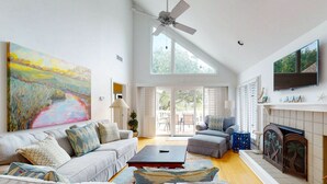 Un salón espacioso con un cuadro grande, ventilador de techo, chimenea y televisor montado en la pared.