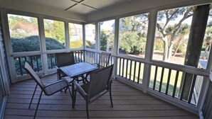 Un patio techado con mesa y sillas, ventanas amplias y vistas a follaje.