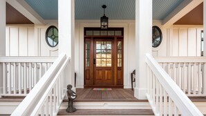 Un porche à l’avant de la maison, avec une porte en bois, des balustrades blanches et une statue.