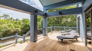 Una terraza de madera con sillones de descanso, baranda de vidrio y vistas a la vegetación.