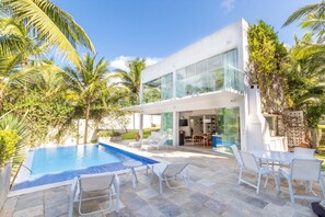 Une maison moderne dotée d’une piscine, de meubles d’extérieur blancs et d’une végétation luxuriante.
