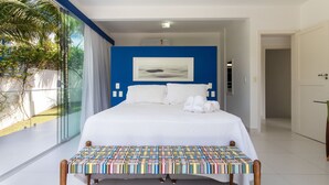 A hotel room with a large bed, a bench with a colorful quilt, a painting on the wall, and a view of greenery outside. - Casa da Árvore - com piscina privativa em Pipa por Carpediem (Tibau do Sul)