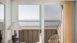 Quarto com vista para a praia, uma cadeira, um abajur e uma mesinha.