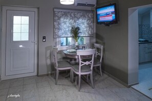 Cozy dining area with a round table and four chairs, a television, and a window with a floral-patterned blind.