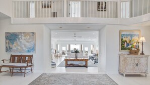A spacious living area with a high ceiling, a central dining table, and a view into the dining room.