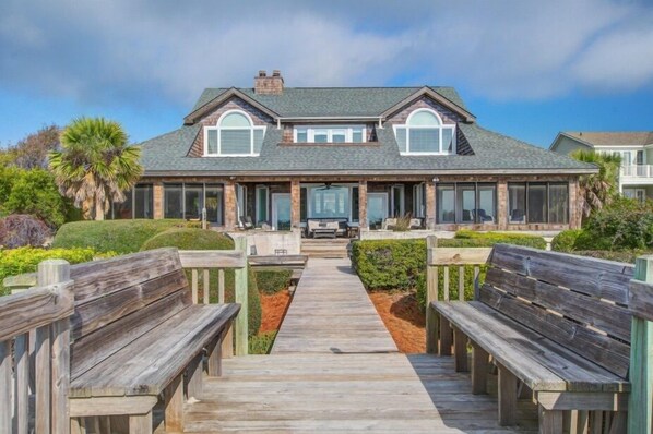 A two-story house with a covered porch, a wooden deck, and a pathway leading to the entrance.