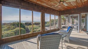 A spacious room with large windows offering ocean views, a ceiling fan, and wicker furniture.