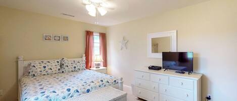 A bedroom with a bed, a dresser, a television, and a ceiling fan.