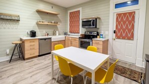 Una cocina funcional con una mesa blanca y sillas amarillas, microondas y estufa.