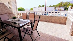 Une terrasse avec une table et des chaises, une piscine en arrière-plan et une clôture blanche.