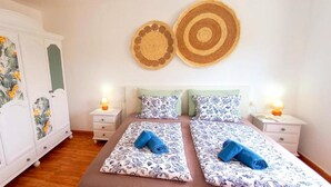 Un lit double avec une literie à motifs floraux, deux tables de chevet avec des lampes, une armoire avec des panneaux à motifs floraux et deux éléments de décoration murale.