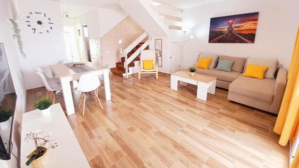 Un salon moderne avec un escalier, un coin repas et un canapé agrémenté de coussins.