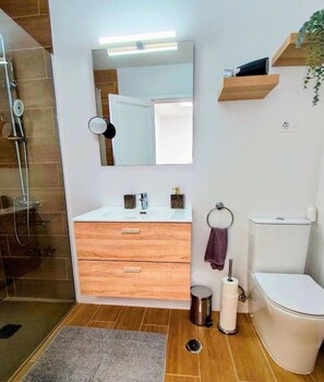Ein modernes Badezimmer mit einem Holzwaschtisch, einem großen Spiegel, einer Toilette und einer Duschkabine.