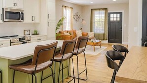 A modern kitchen with white cabinets, a microwave, and a stove. There is a dining area with a wooden table and chairs. - The Modern Historic Gem | Just minutes to Downtown (West Columbia)