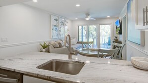 Uma cozinha moderna com bancada de mármore, pia de aço inoxidável e área de jantar com mesa e cadeiras de vidro.