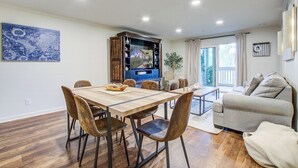 A dining area with a wooden table and chairs, a kitchen area with cabinets, and a living area with a sofa and a plant. - Seabrook Exclusives | 2011 Marsh Walk (Seabrook Island)