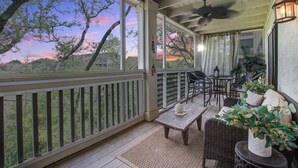 A covered porch with a view of trees and a sunset, featuring a table and chairs, a ceiling fan, and a potted plant. - Seabrook Exclusives | 2011 Marsh Walk (Seabrook Island)