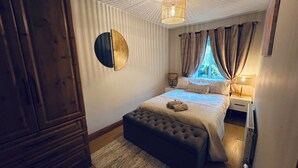 Un dormitori amb un llit, una tauleta de nit, una làmpada, una decoració circular a la paret i una finestra amb cortines.