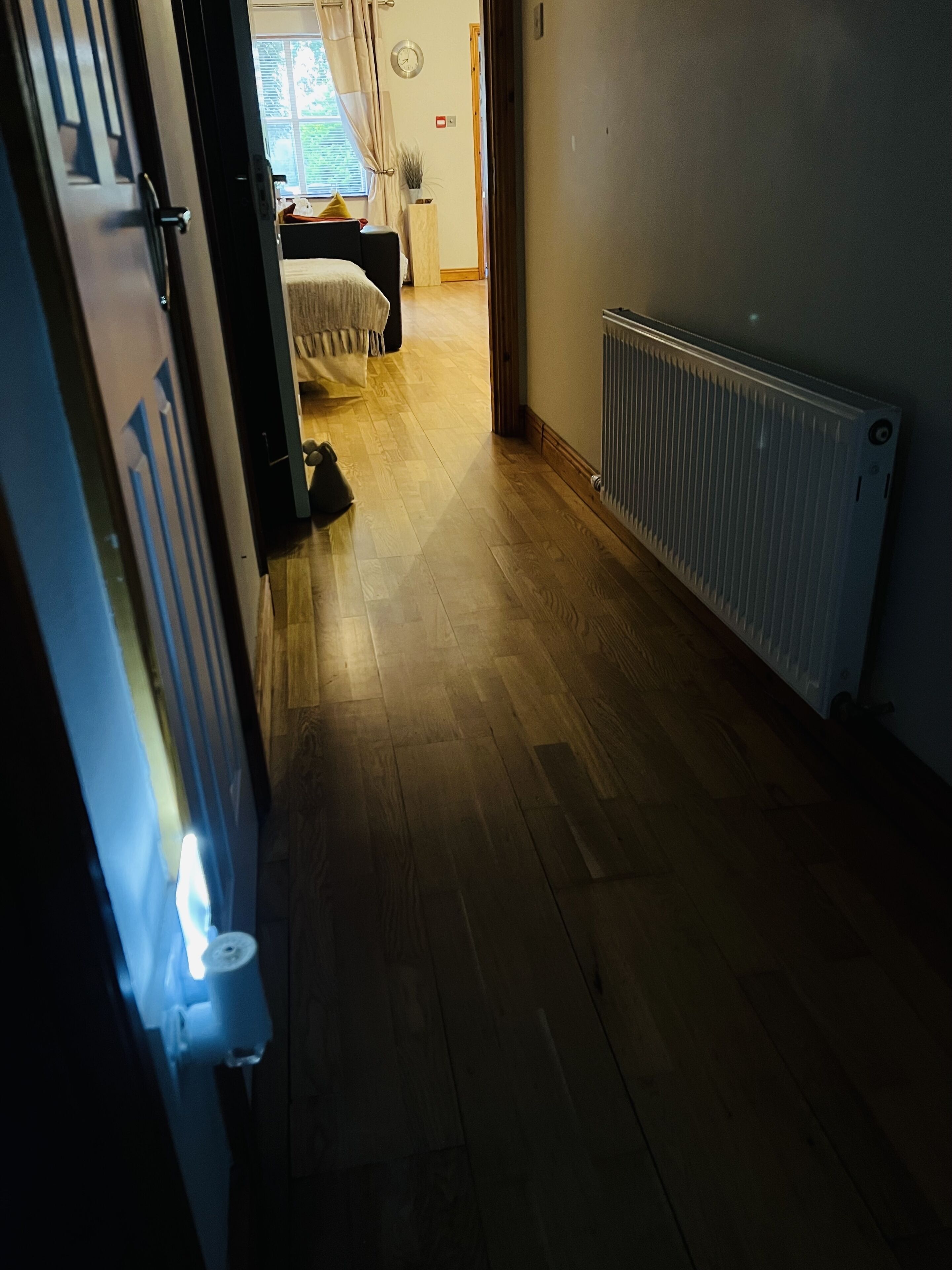 A hallway with wooden flooring, a radiator, and a bed in the background.