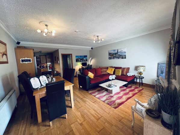 A cozy living room with a wooden dining table, a red sofa, and a patterned rug.
