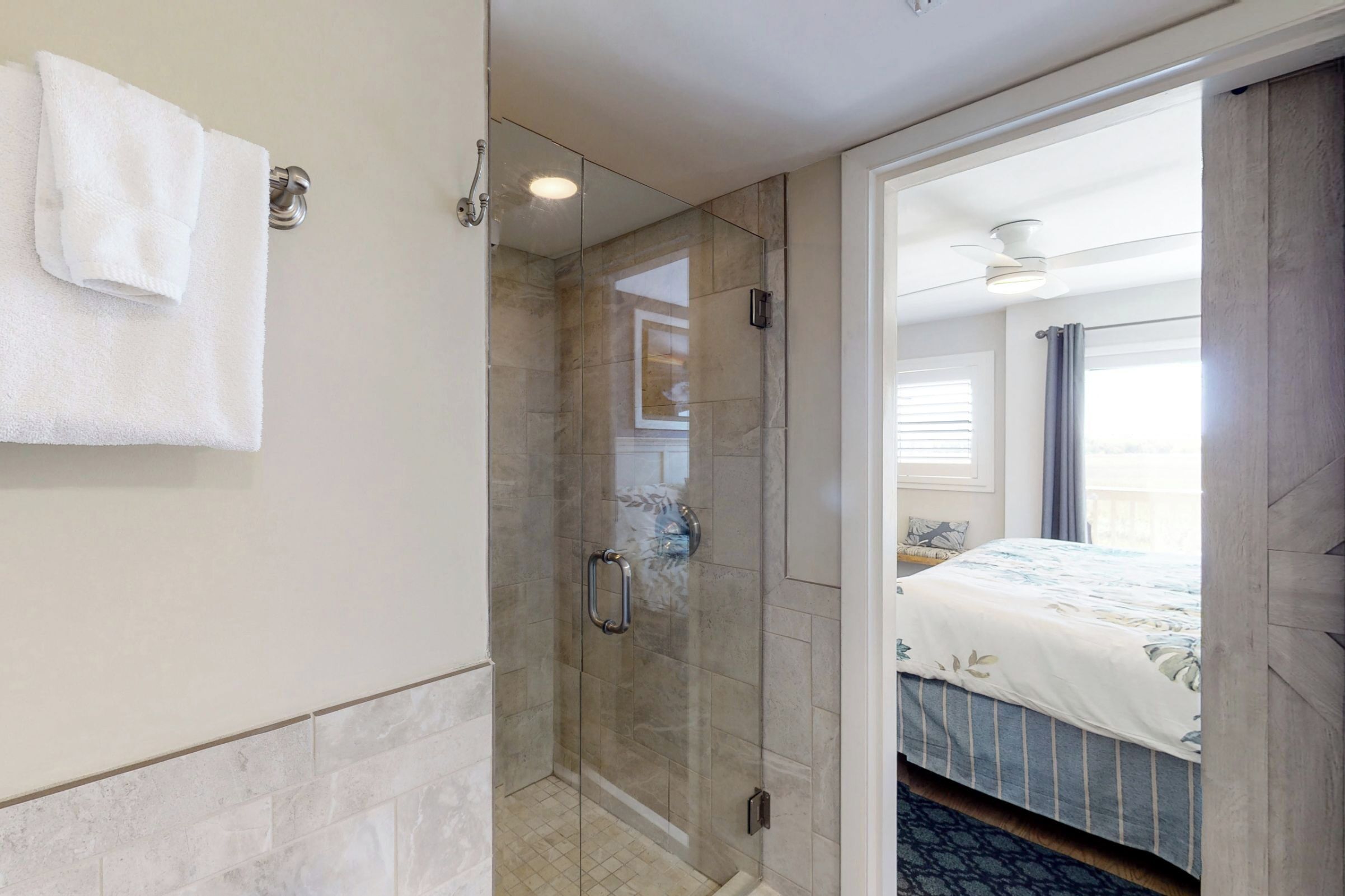 Ein Hotelzimmer mit einer gläsernen Dusche, einem Bett mit floralem Überwurf und Blick ins Freie.
