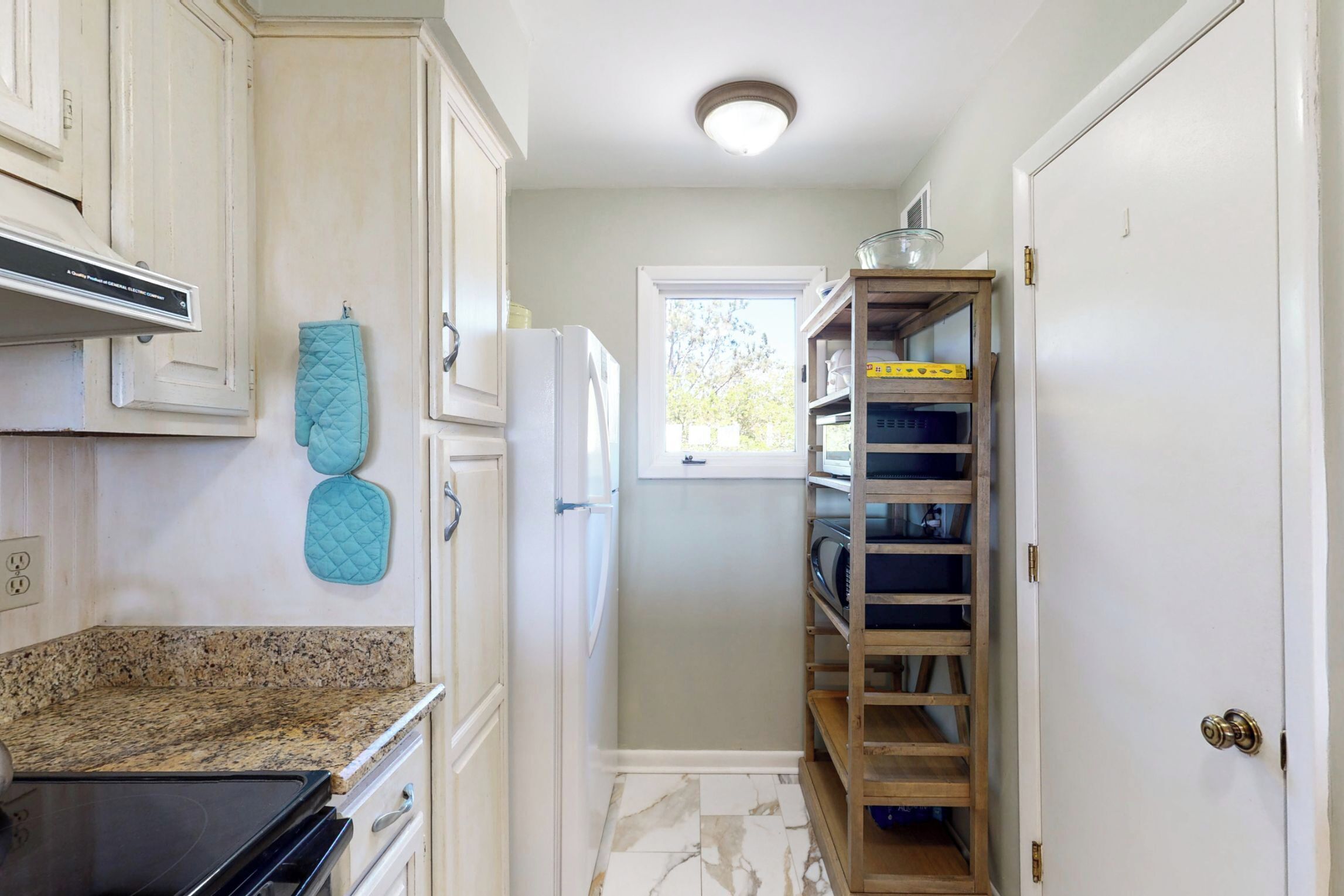 A kitchen with white cabinets, a granite countertop, a teal oven mitt, a white refrigerator, and a wooden shelving unit with storage boxes.