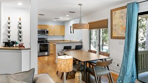A modern kitchen with wooden cabinets, stainless steel appliances, and a dining area with a wooden table and chairs. - Seabrook Exclusives | 2764 Live Oak Villa (Seabrook Island)