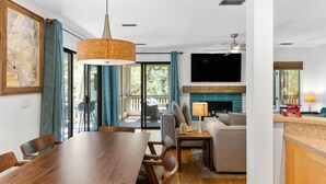 A modern living room with a wooden dining table, a sofa, a TV, and a fireplace. - Seabrook Exclusives | 2764 Live Oak Villa (Seabrook Island)