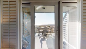 Une porte-fenêtre coulissante donnant sur un balcon aménagé avec du mobilier d’extérieur et offrant une vue sur le paysage.