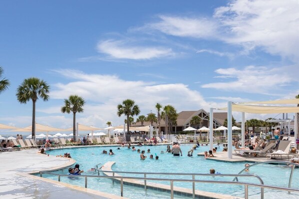 A large outdoor swimming pool with palm trees, lounge chairs, and umbrellas.