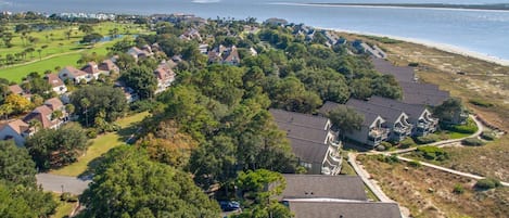An aerial view of a coastal residential area with houses, a beach, and a golf course.