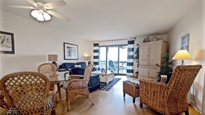 A spacious living room with wicker furniture, a ceiling fan, and a view to the outside. - Seabrook Exclusives | 1377 Pelican Watch (Johns Island)