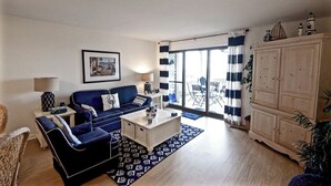 A living room with a blue sofa, a white coffee table, and a wooden cabinet. - Seabrook Exclusives | 1377 Pelican Watch (Johns Island)